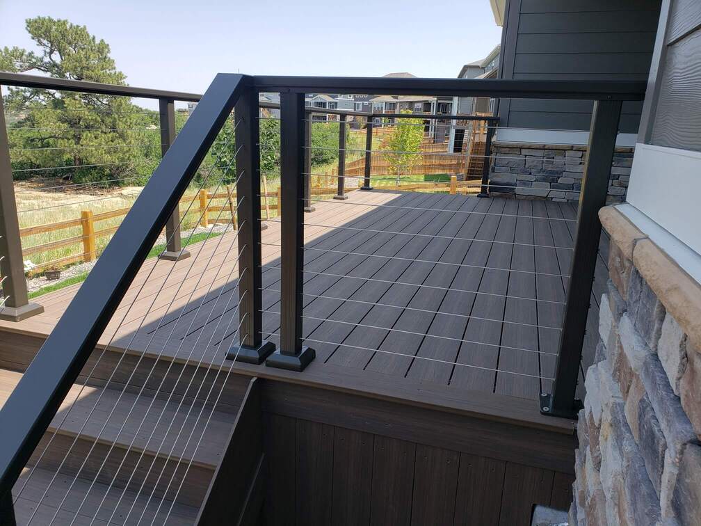 A modern composite deck with black metal and cable railings featuring wood-look decking and a staircase leading to the lower level