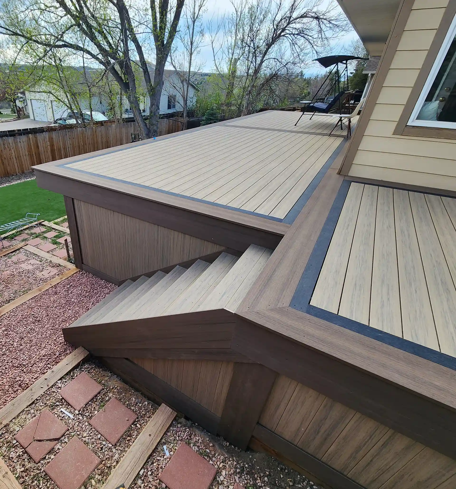 Multi-level composite deck with contrasting border design, integrated stairs, and a landscaped backyard view.