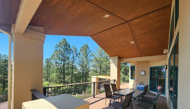 Covered deck with composite flooring, black metal railings, and an outdoor seating area overlooking a wooded landscape