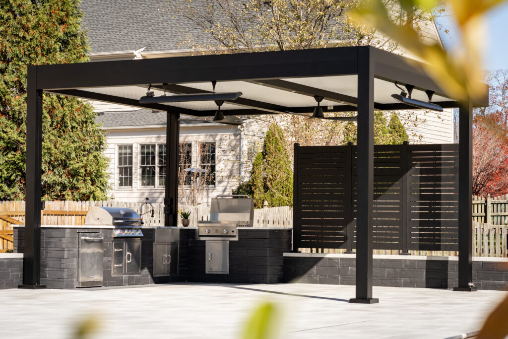 Modern black aluminum pergola with insulated roof, ceiling fans, outdoor heaters, and custom outdoor kitchen in a luxury residential backyard.