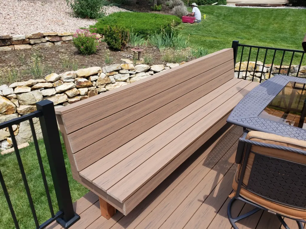 brown-bench-on-the-custom-deck-with-black-metal-railings-and-outdoor-living-dining-set-area-featuring-a-person-cutting-grass-in-castle-rock-co