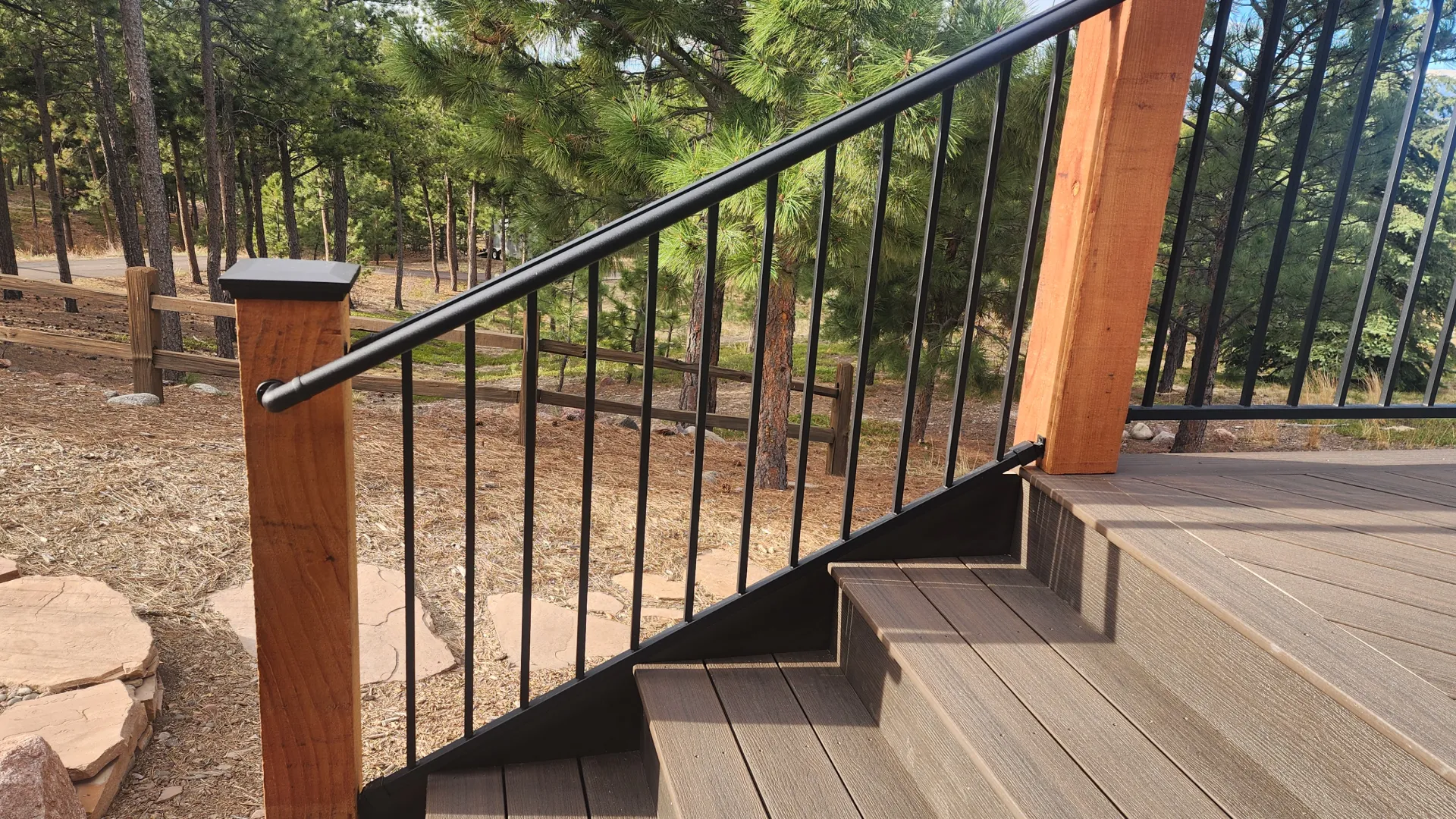 composite-deck-with-black-metal-railing-on-staircase-featuring-agricultural-wooden-fence-and-big-trees-on-the-background-in-castle-rock-co