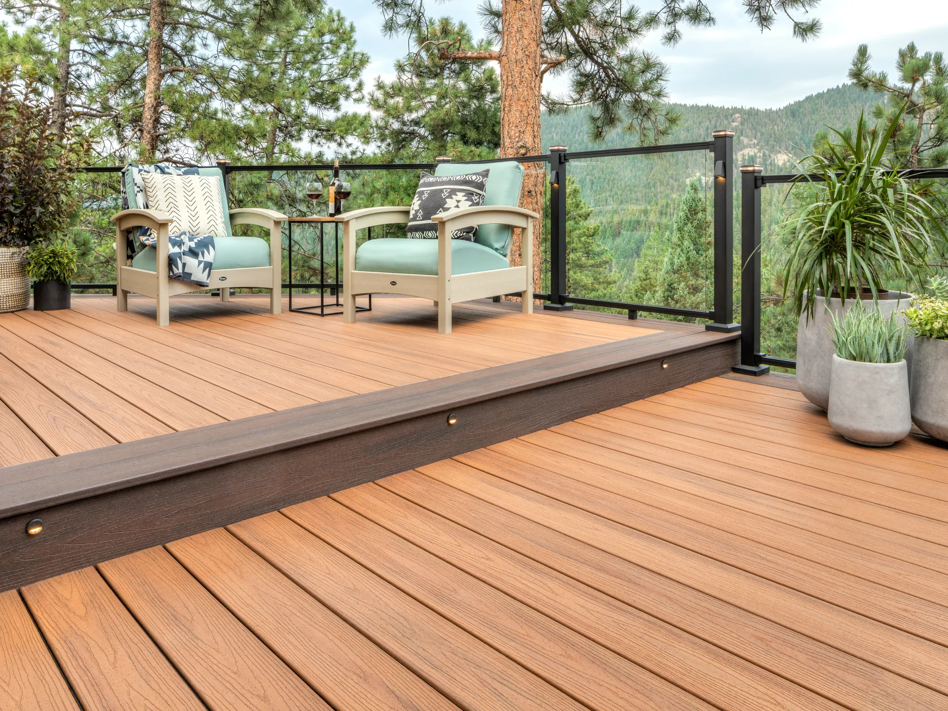 custom-deck-with-lights-on-stair-with-outdoor-chairs-and-potted-plants-featuring-glass-railings-and-post-cap-lights-with-nature-view-in-castle-rock-co