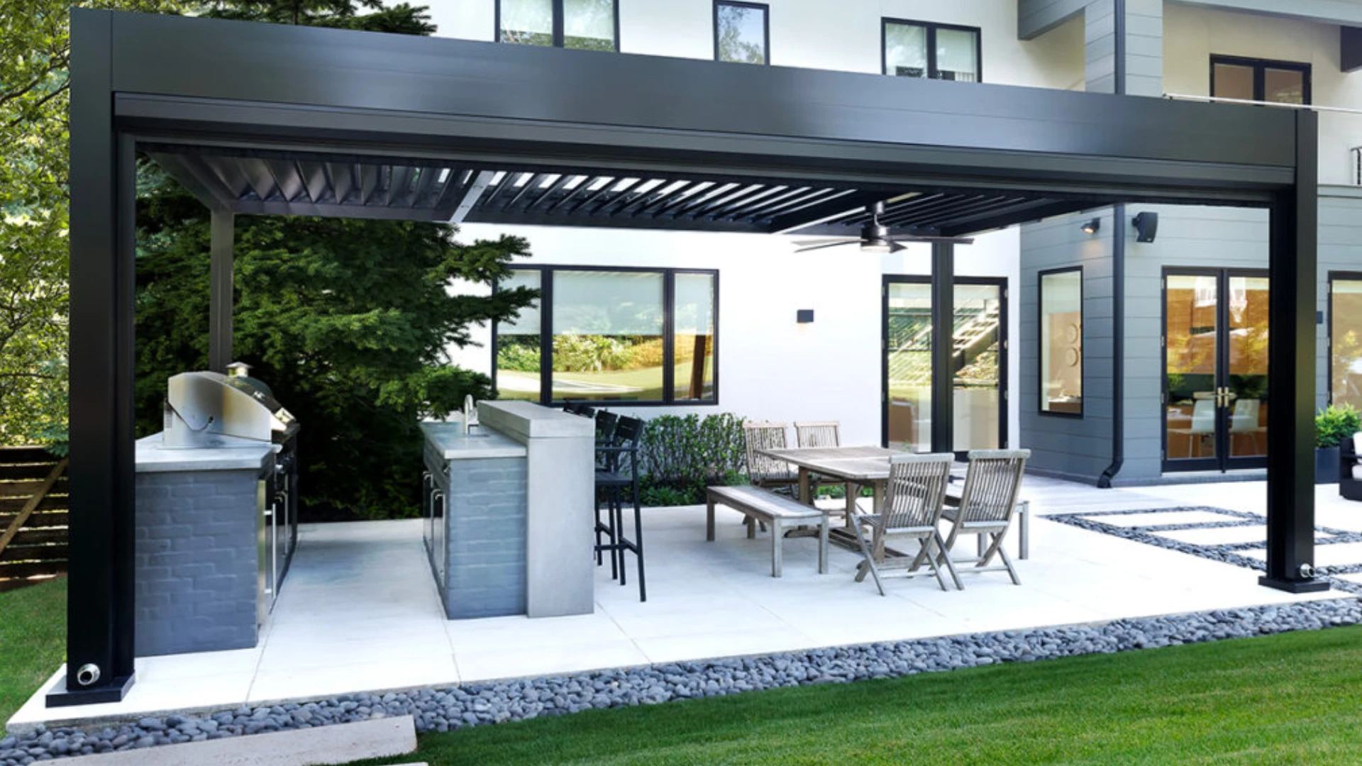 outdoor-living-kitchen-and-dining-set-under-the-louvered-pergola-with-a-fan-on-the-luxury-house-with-multiple-windows-with-trees-on-the-side-in-castle-rock-co