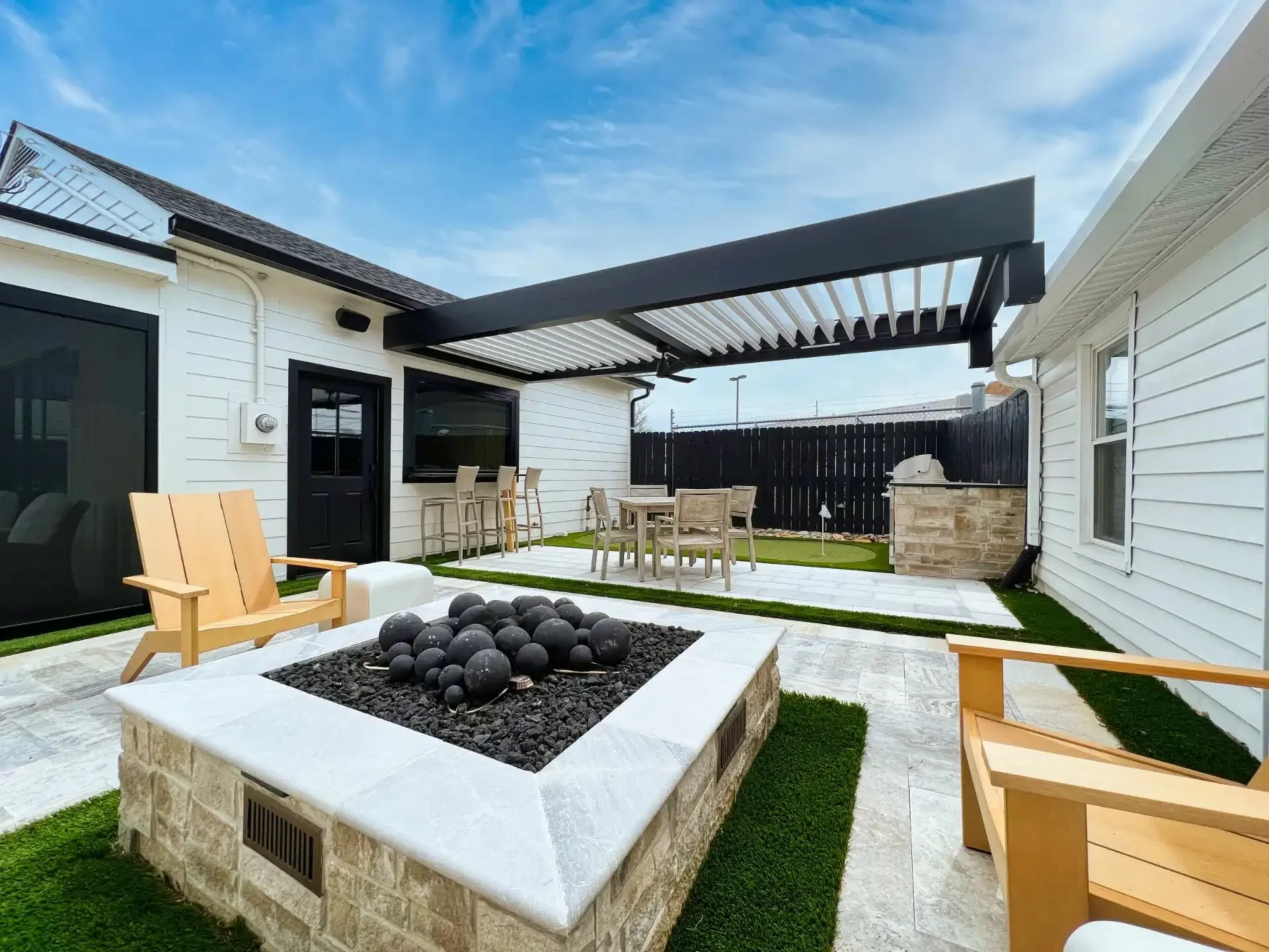 patio-featuring-a-fire-pit-with-two-wooden-chairs-and-outdoor-living-dining-set-area-and-black-picket-privacy-fence-on-the-white-modern-house-in-castle-rock-co