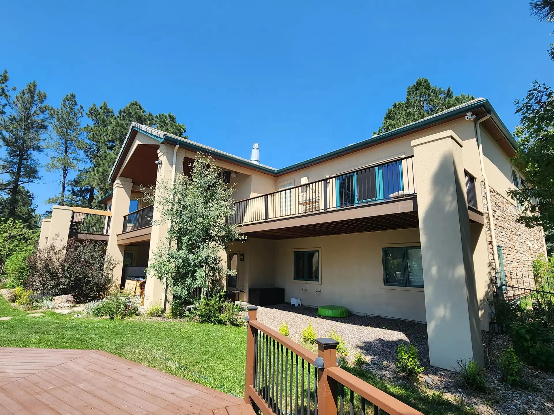 residential-building-with-under-deck-with-black-metal-railing-surrounded-by-grass-plants-and-trees-with-blue-sky-view-on-the-background-in-castle-rock-co
