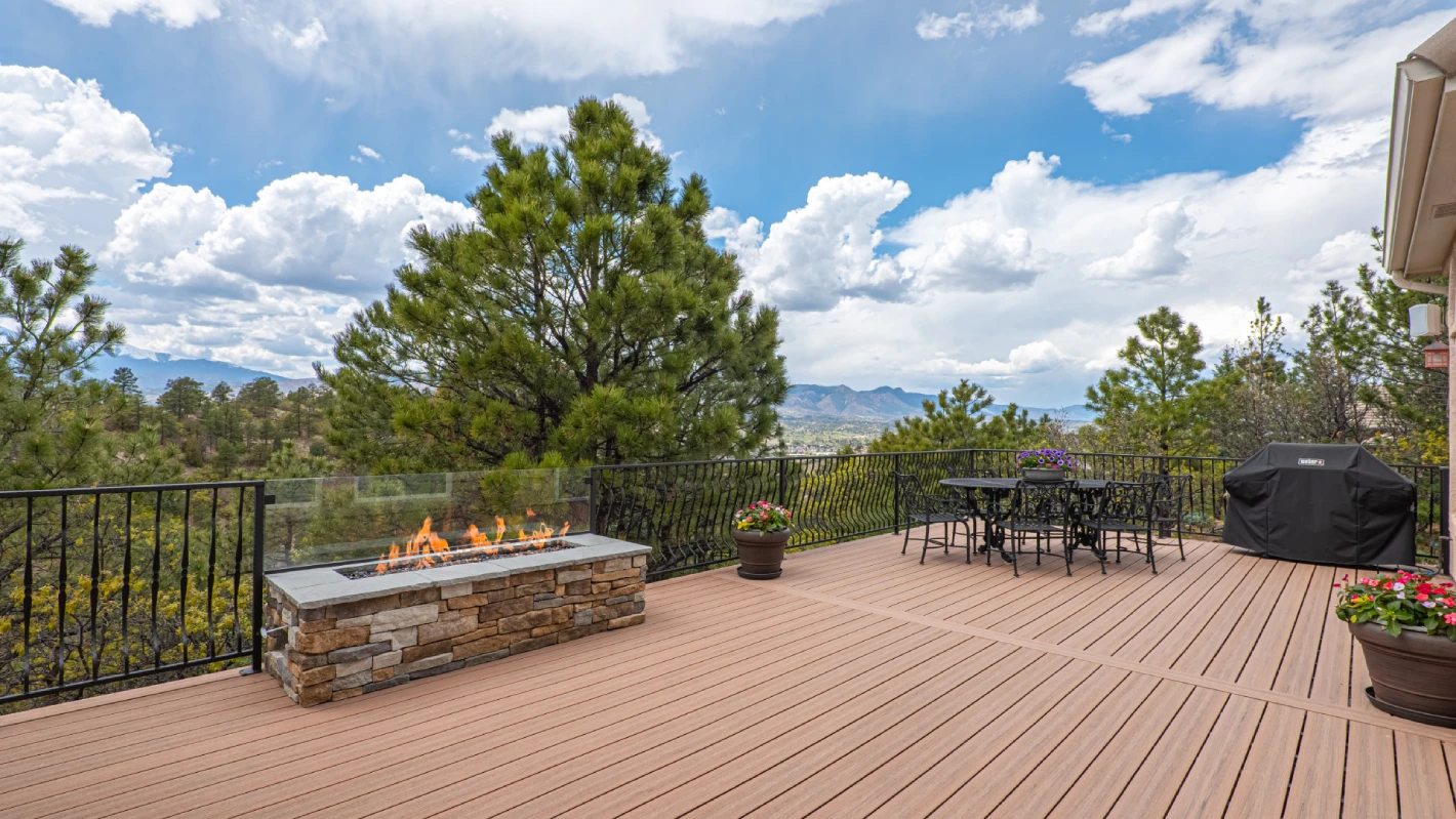 residential-deck-with-outdoor-living-dining-area-and-covered-grill-with-potted-plants-and-firepit-with-black-metal-railings-featuring-trees-cloudy-sky-and-city-view-in-castle-rock-co
