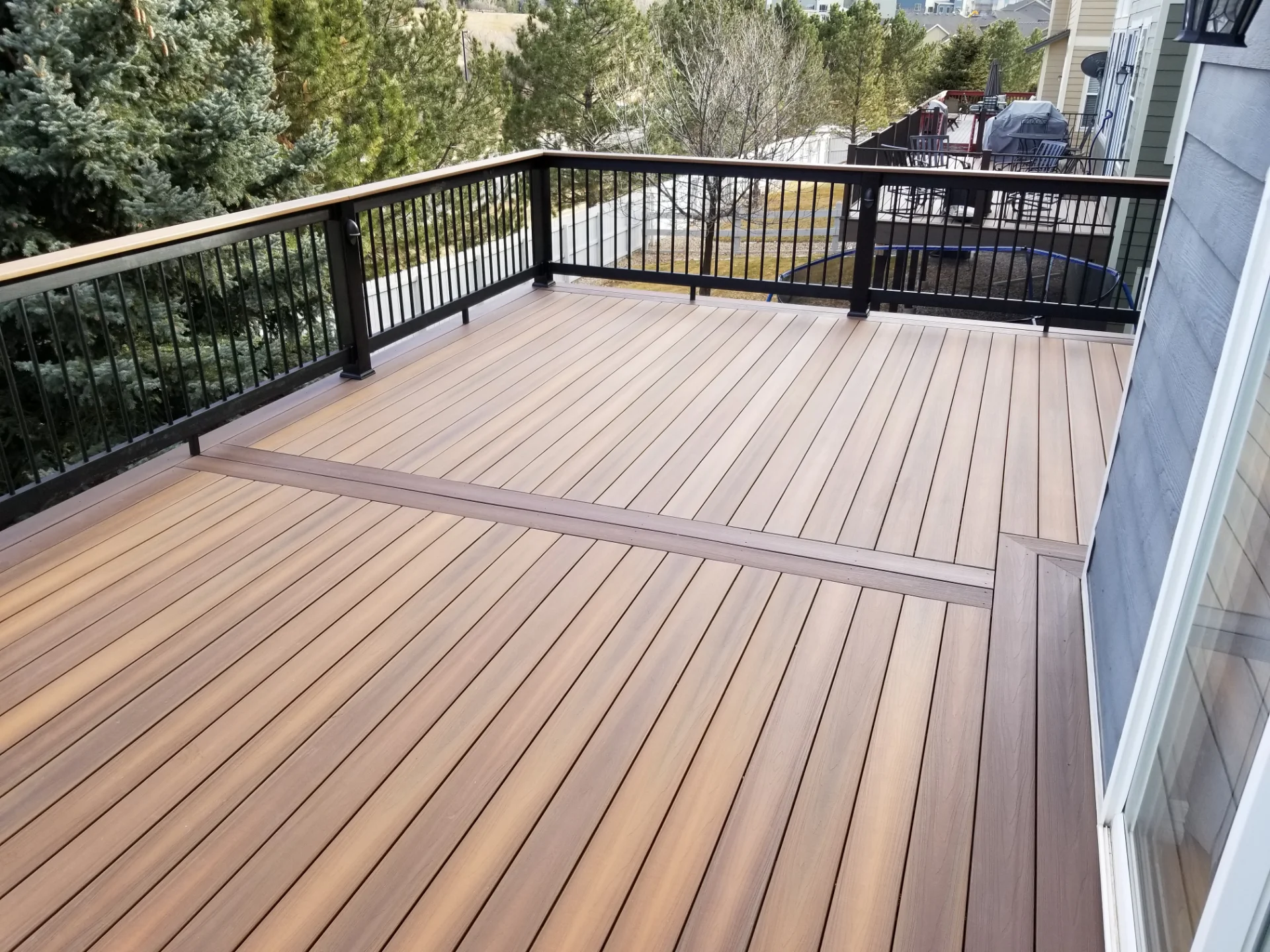 spacious-deck-installation-with-black-metal-railings-and-trees-with-white-vinyl-wall-fence-on-the-background-in-castle-rock-co