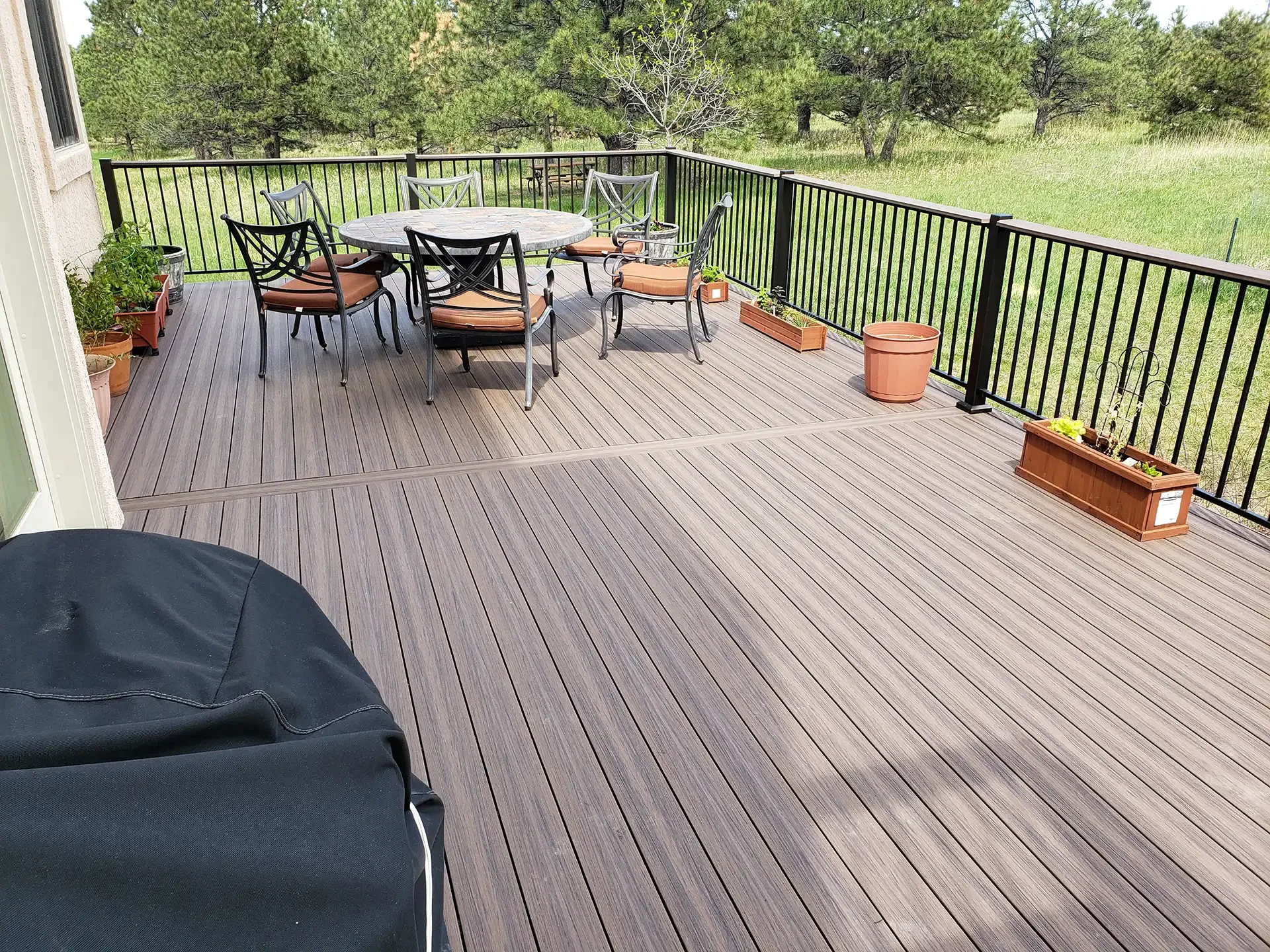 spacious-deck-with-outdoor-living-dining-set-and-black-metal-railing-with-decorative-potted-plants-and-big-tree-on-the-background-in-castle-rock-co
